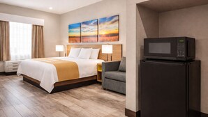 A hotel room with a bed, a gray armchair, a TV on a stand, and a painting on the wall. - Days Inn & Suites by Wyndham Tomball/Houston NW (Tomball)