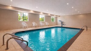 An indoor swimming pool with clear water, surrounded by beige walls and windows. - Days Inn & Suites by Wyndham Tomball/Houston NW (Tomball)