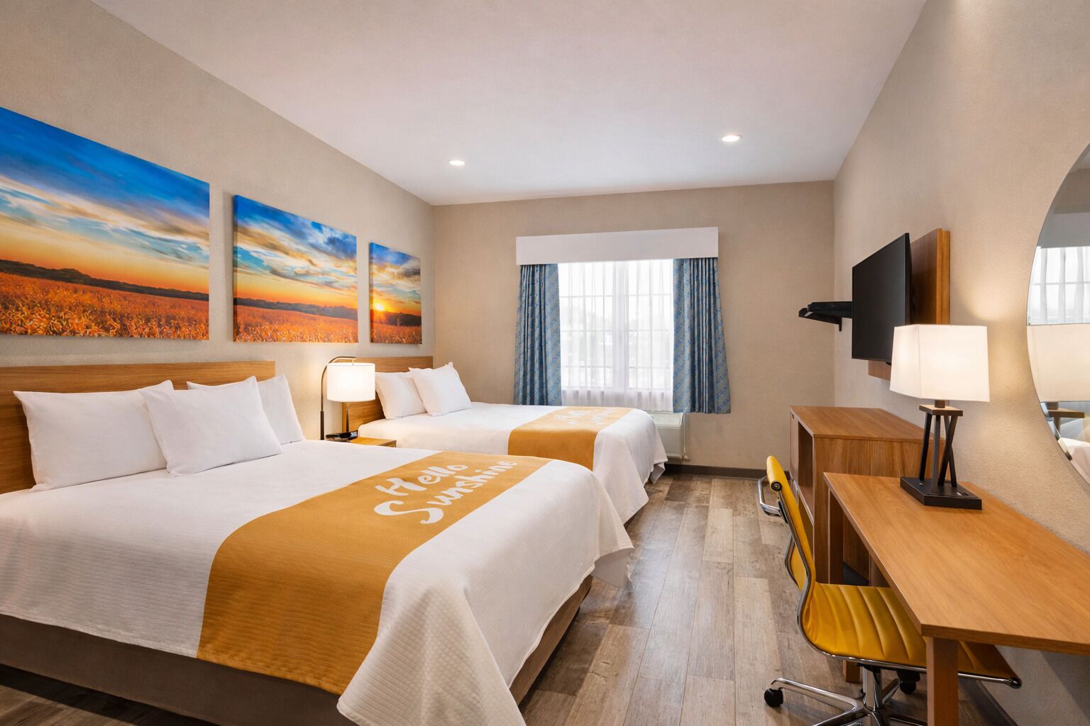 Hotelkamer met twee bedden, een bureau, een stoel, een televisie en kunstwerken aan de wand.