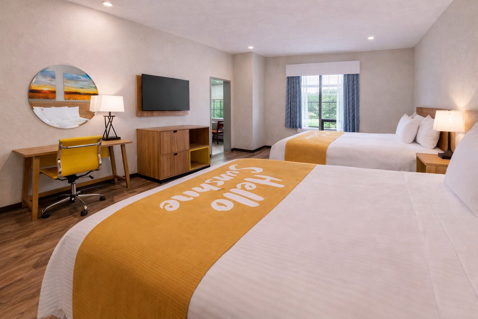 A hotel room with two beds, a desk, a chair, a TV, and a window with curtains.