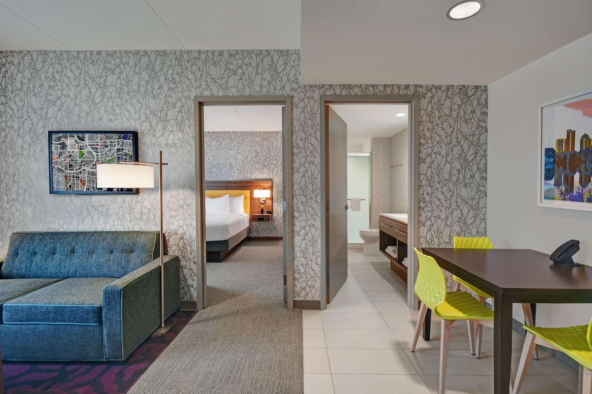 A hotel room with a bed, a desk, a chair, a sofa, and a painting on the wall.