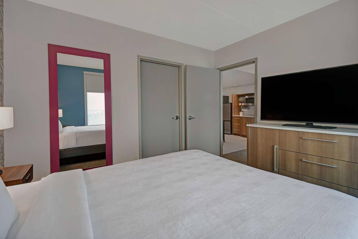A hotel room with a bed, a television, a wardrobe, and a mirror.