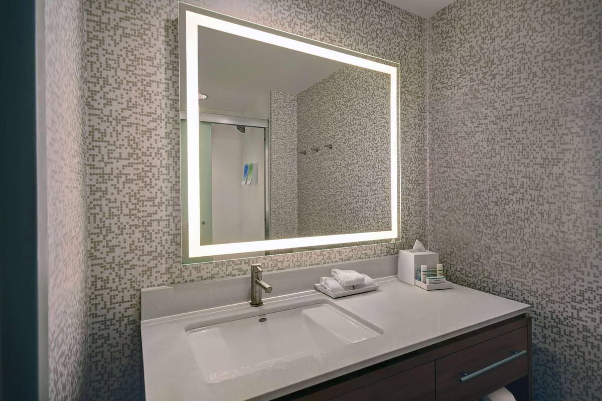A modern bathroom with a large mirror, a sink, and a shower.