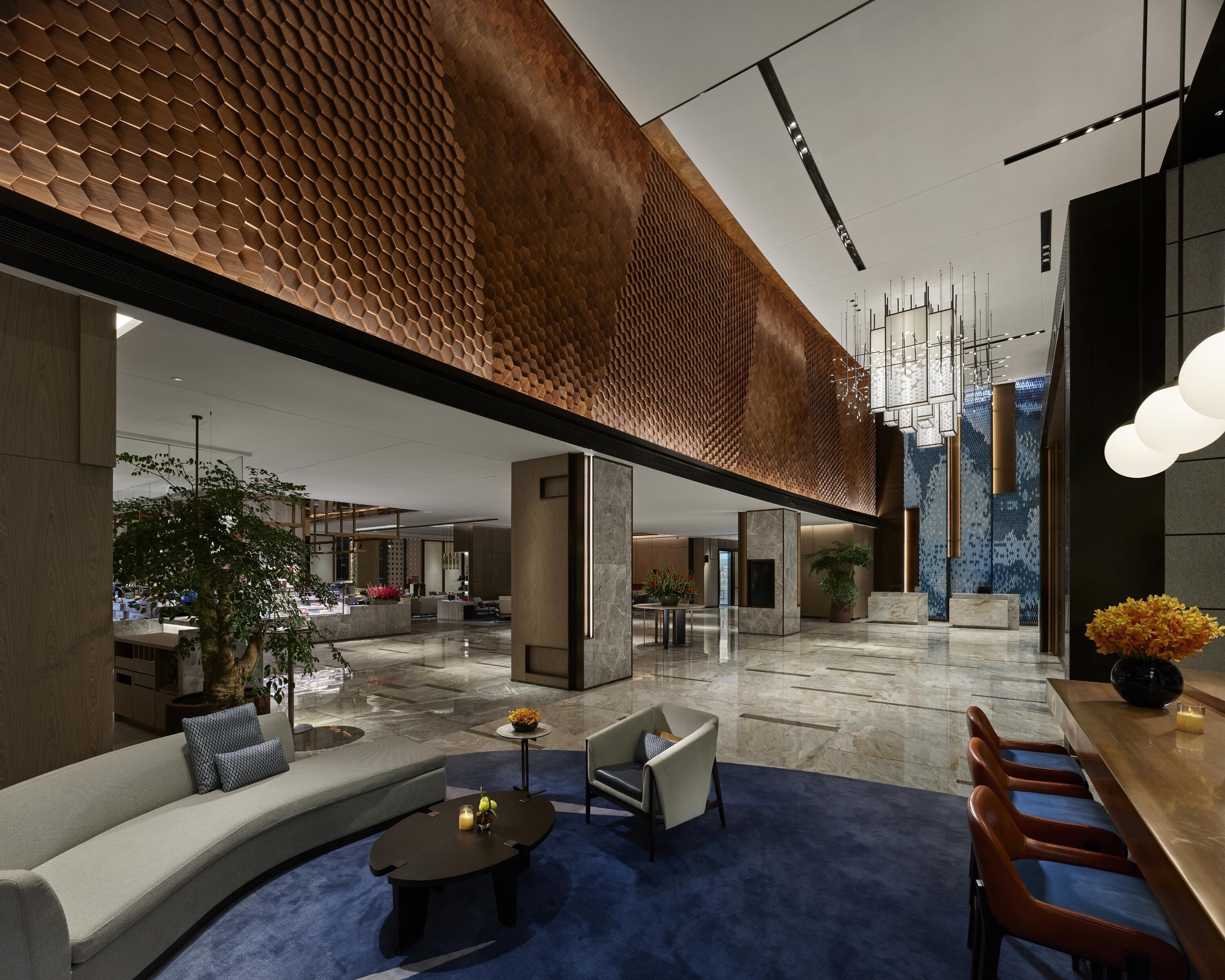 A modern lobby with a geometric ceiling design, seating areas, and a reception desk.