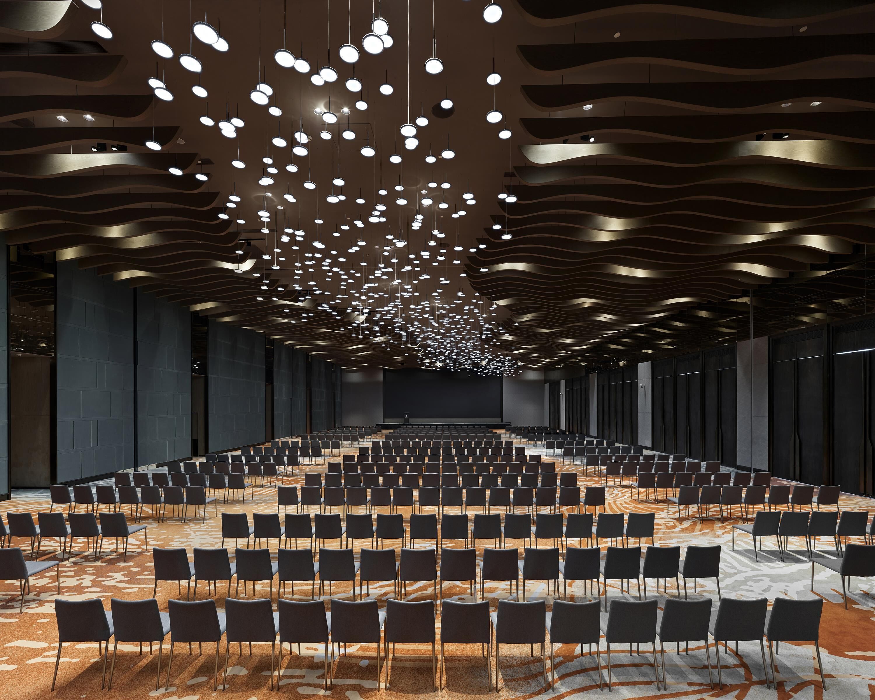 A conference room with rows of chairs, a patterned carpet, and a ceiling with hanging lights.