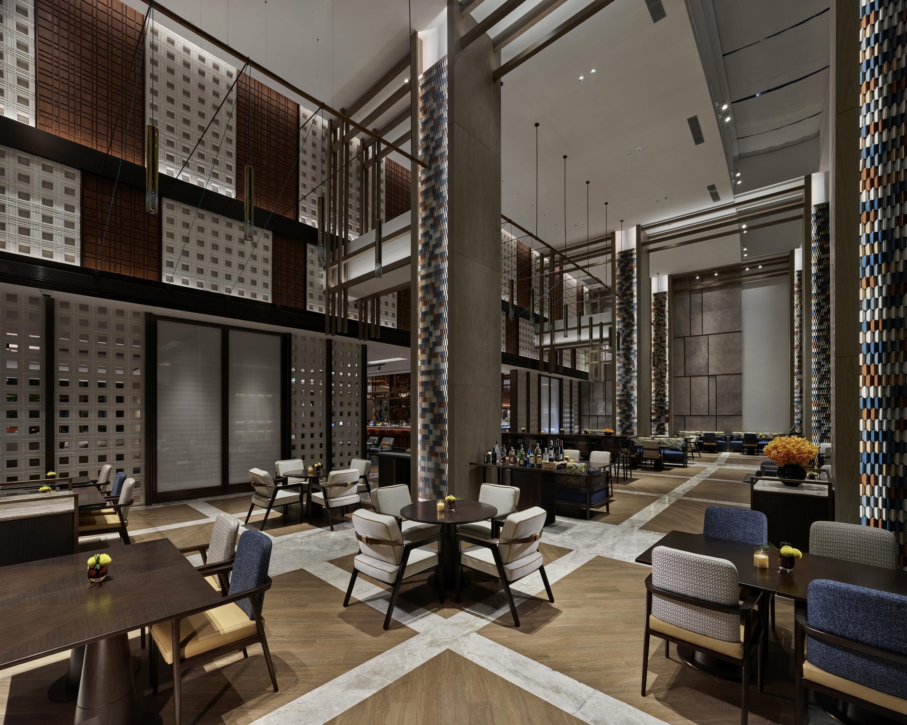 Un lobby de hotel moderno con techos altos, un área de estar central y un bar.
