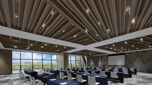 A conference room with a modern ceiling design, large windows with a city view, and a patterned carpet.