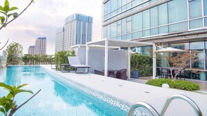A modern hotel pool area with lounge chairs and a covered seating area, surrounded by high-rise buildings.