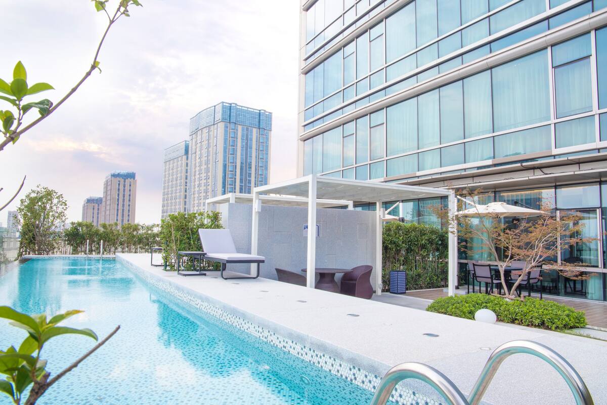 A modern hotel pool area with lounge chairs and a covered seating area, surrounded by high-rise buildings.