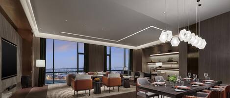 A modern hotel room with a panoramic city view, a dining area with a long table, and a cozy seating area with sofas and chairs.