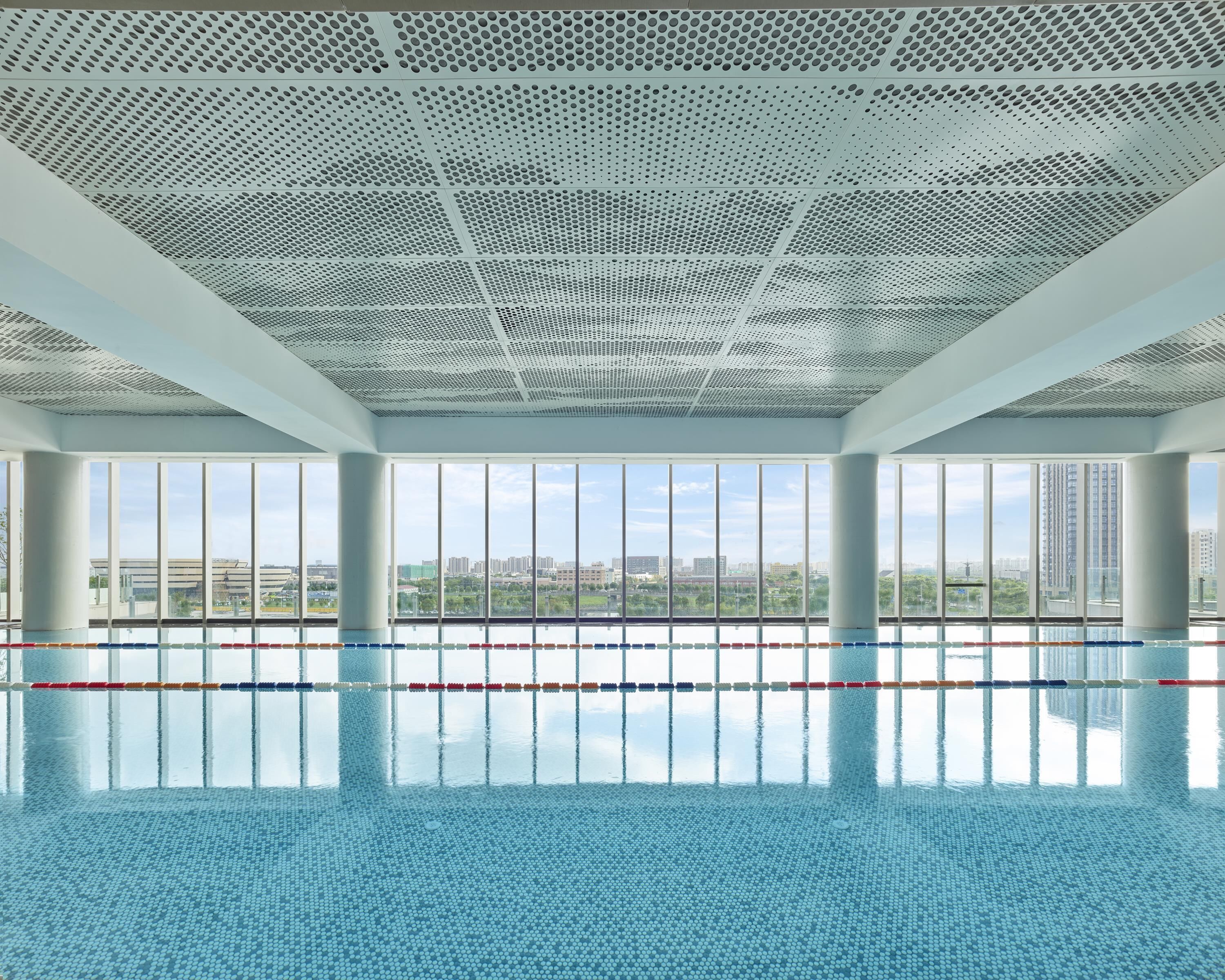 A large indoor swimming pool with clear views of a cityscape through large windows.