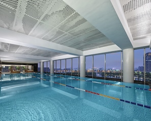 An indoor swimming pool with clear water, a ceiling with a perforated pattern, and large windows offering a city view. - Hyatt Regency Shanghai Songjiang (Shanghai)
