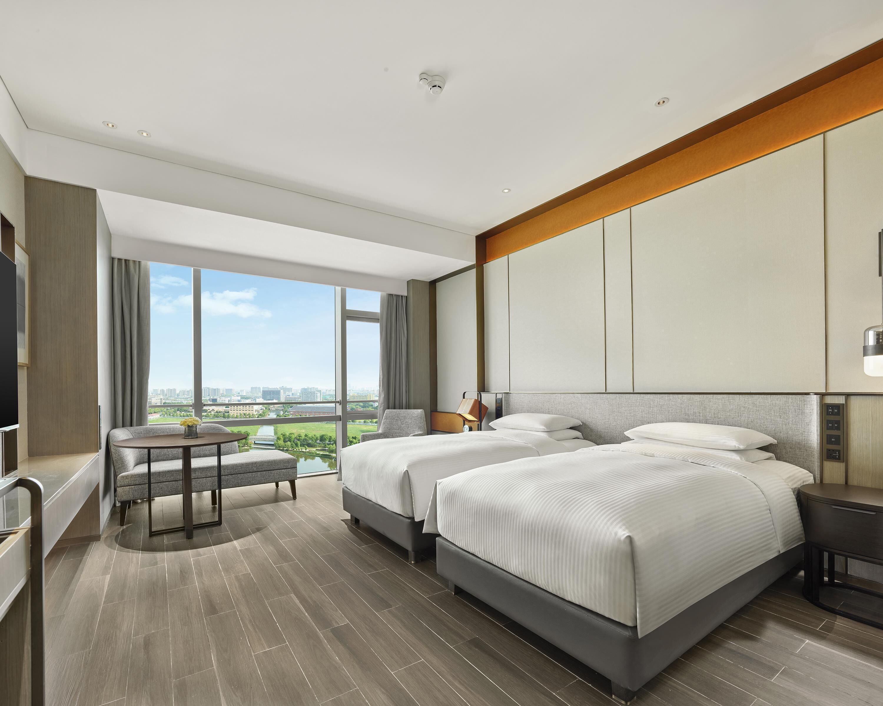 A modern hotel room with a large bed, a seating area, and a view of the city.