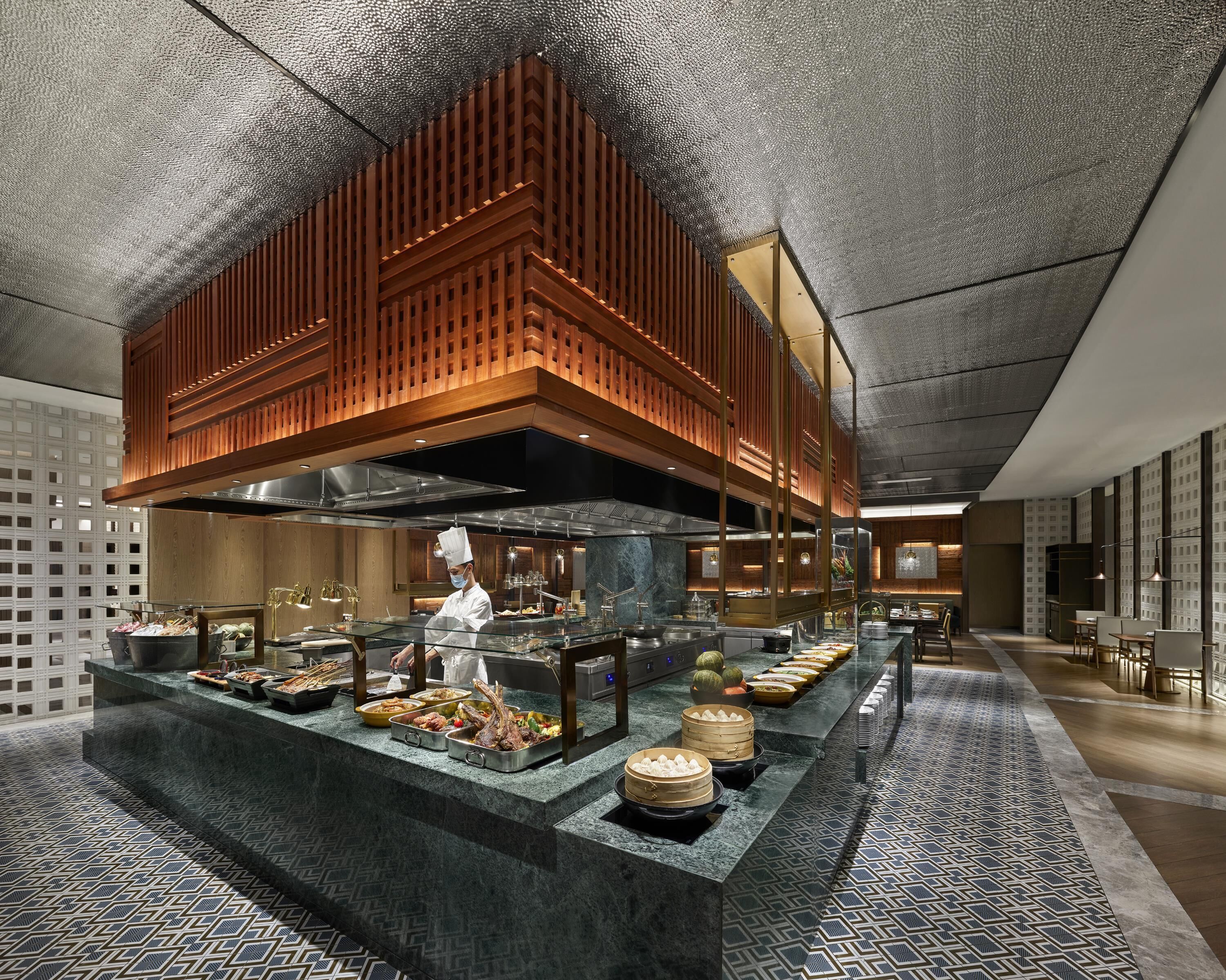 Una cucina moderna con uno chef che prepara piatti, un buffet ricco di varie pietanze e un pavimento decorato.