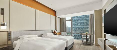 A modern hotel room with two beds, a desk, a chair, a small table with a vase, and a large window offering a city view.