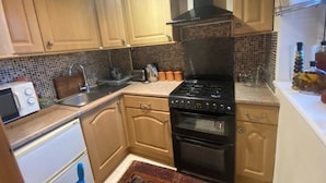 A kitchen with wooden cabinets, a black stove, a microwave, and a sink. - 2-bed Apartment in High Wycombe Private Garden (High Wycombe)