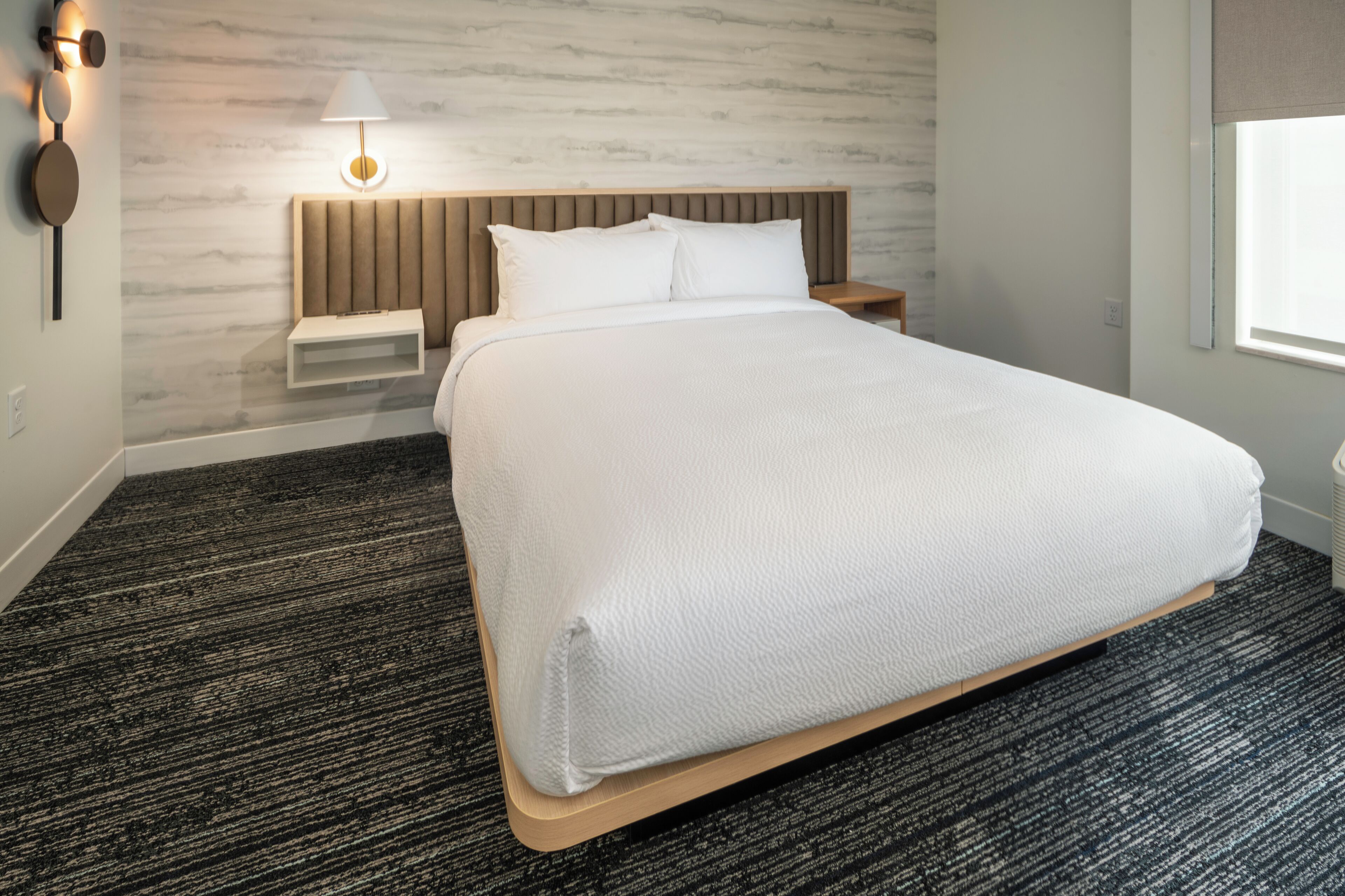 Une chambre d’hôtel moderne avec un grand lit, une table de chevet, une lampe fixée au mur et une fenêtre donnant sur un beau paysage.