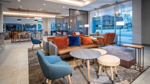 Een moderne loungehoek met zitplaatsen, tafels en uitzicht op de stad door grote ramen.
