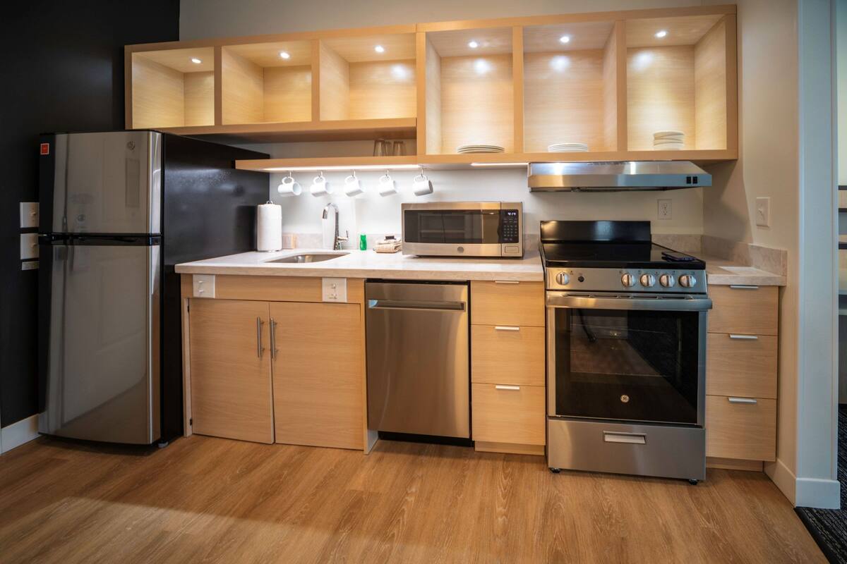 Une cuisine moderne dotée d’appareils électroménagers en acier inoxydable, de meubles en bois et d’un four à micro-ondes encastré.