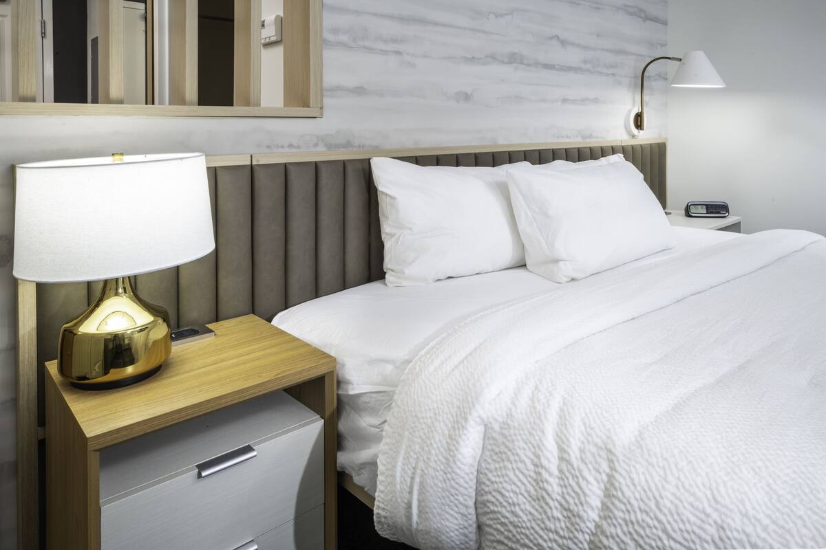 Une chambre d’hôtel comprenant un lit, une table de chevet avec une lampe, une commode et un miroir.