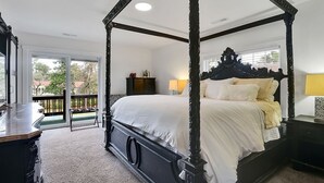 A four-poster bed with a white bedspread, a nightstand with a lamp, and a view of the outdoors through a sliding door.