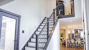 A modern interior with a staircase leading to a loft area, a dining area with chairs, and a kitchen in the background.