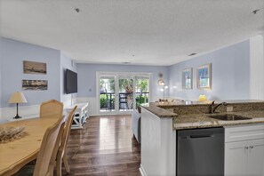 A modern kitchen with a granite countertop, built-in dishwasher, and a dining area with a wooden table and chairs.