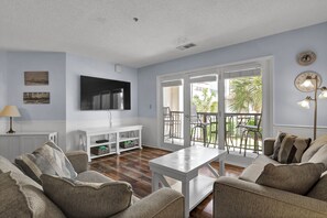 A living room with a television, sofa, coffee table, and a view of the outdoors.