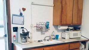 Een keuken met houten kastjes, een wit aanrecht, een koffiezetapparaat, een magnetron en een kalender aan de muur.