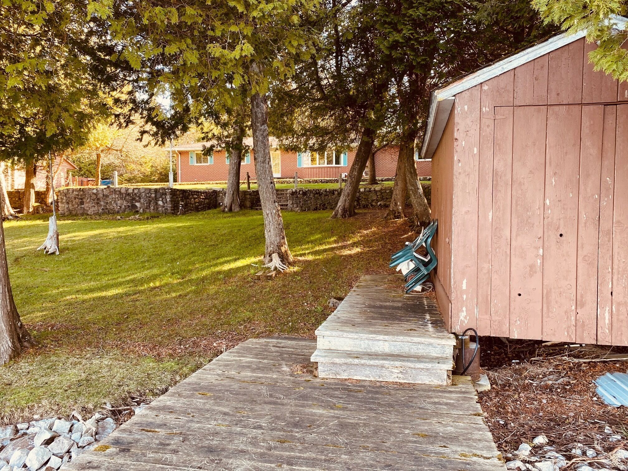 A wooden shed with a concrete pathway leading to it, surrounded by trees and a grassy area.