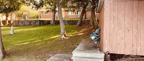 A wooden shed with a concrete pathway leading to it, surrounded by trees and a grassy area.