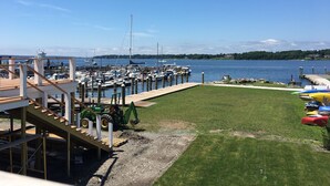 A marina with boats docked, a grassy area with kayaks, and a clear blue sky.