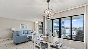 Amplia sala de estar con mesa de comedor, sofá azul y un balcón con vistas a la ciudad.