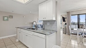 Una cocina moderna con armarios blancos, lavavajillas integrado y un amplio ventanal con vistas a la ciudad.