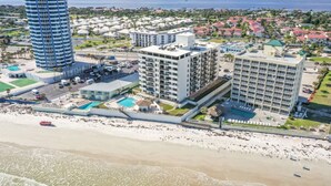 Un hotel frente al mar con varias construcciones, una playa y una extensa masa de agua al fondo.