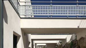 Ein Korridor mit einem Holzboden, der zu einem Gebäude mit weißer Fassade und einem Balkon mit Geländer führt.
