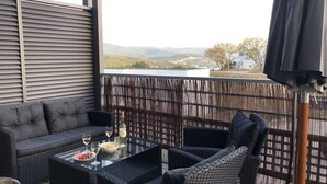 Ein Balkon mit einer Sitzecke, Korbstühlen und einem Glastisch mit einer Flasche und einer Obstschale.
