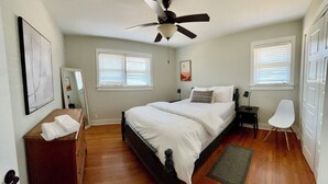 Ein Schlafzimmer mit einem Bett, Nachttischen, einem Sessel, einem Deckenventilator und einem Fenster mit Jalousien.