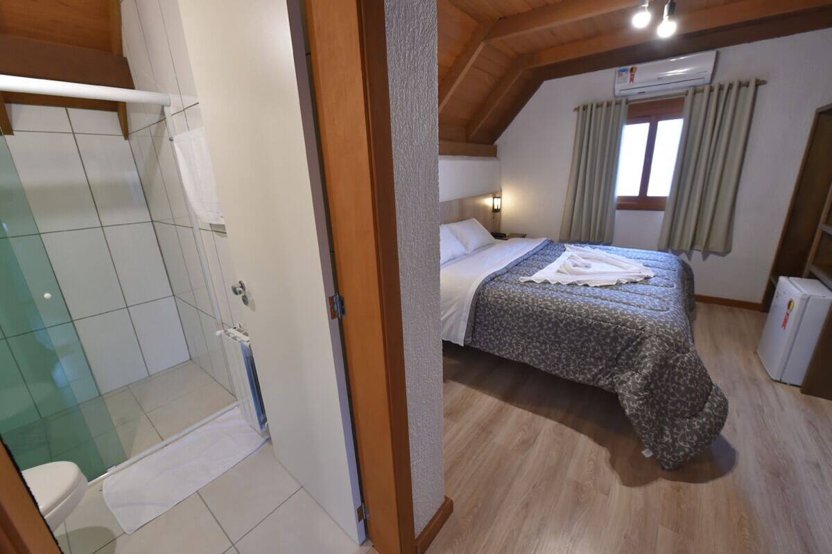 A bedroom with a bed, a nightstand, a window with curtains, and a small refrigerator.