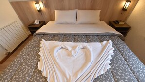 A neatly made bed with a patterned bedspread, two bedside lamps, a bedside phone, and a radiator. - Hotel Villa Aconchego (Gramado)