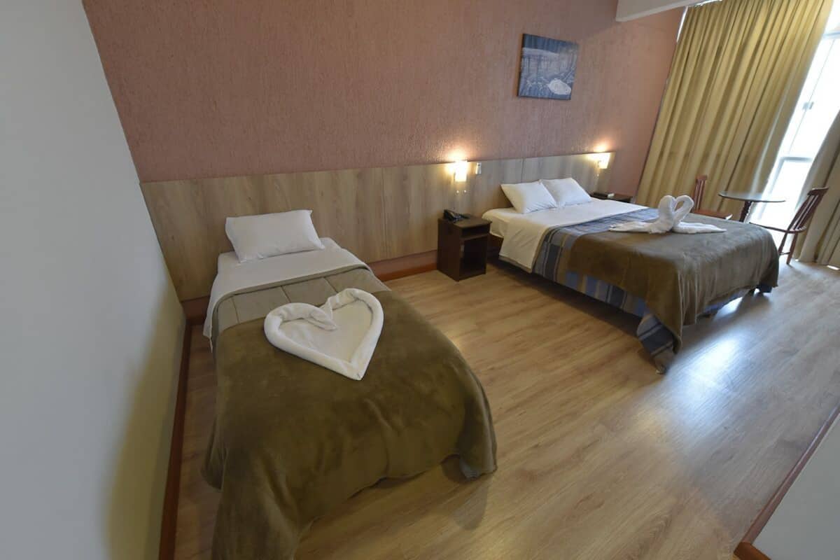 A hotel room with two single beds, a wooden headboard, a small table, and a chair.