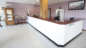 A reception area with a white reception desk, a wooden pillar, a refrigerator, and a wall-mounted clock. - Hotel Villa Aconchego (Gramado)