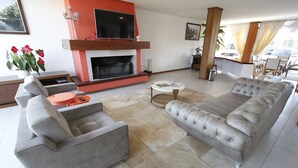 A modern living room with a fireplace, grey sofas, a coffee table, and a TV. - Hotel Villa Aconchego (Gramado)