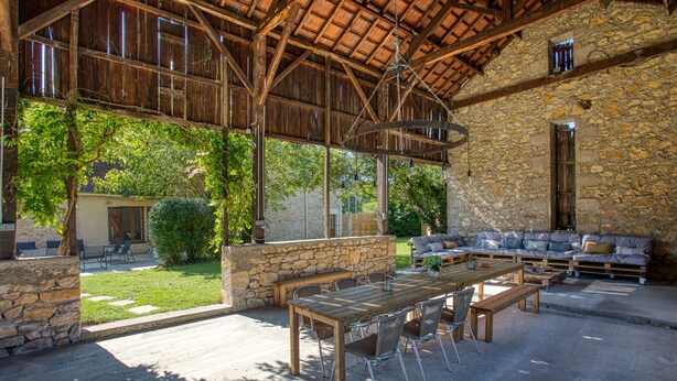 Une terrasse extérieure avec une table et des chaises en bois, des murs en pierre et un bâtiment en pierre en arrière-plan.