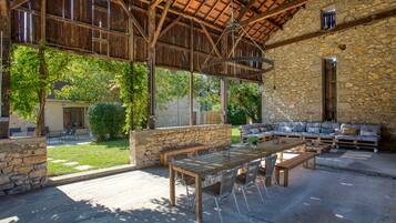An outdoor patio with a wooden table and chairs, stone walls, and a stone building in the background.