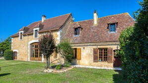 Une maison en pierre avec un toit de tuiles, un petit jardin et un ciel bleu dégagé.