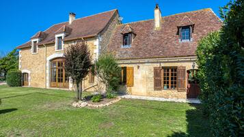 A stone house with a tiled roof, a small garden, and a clear blue sky.