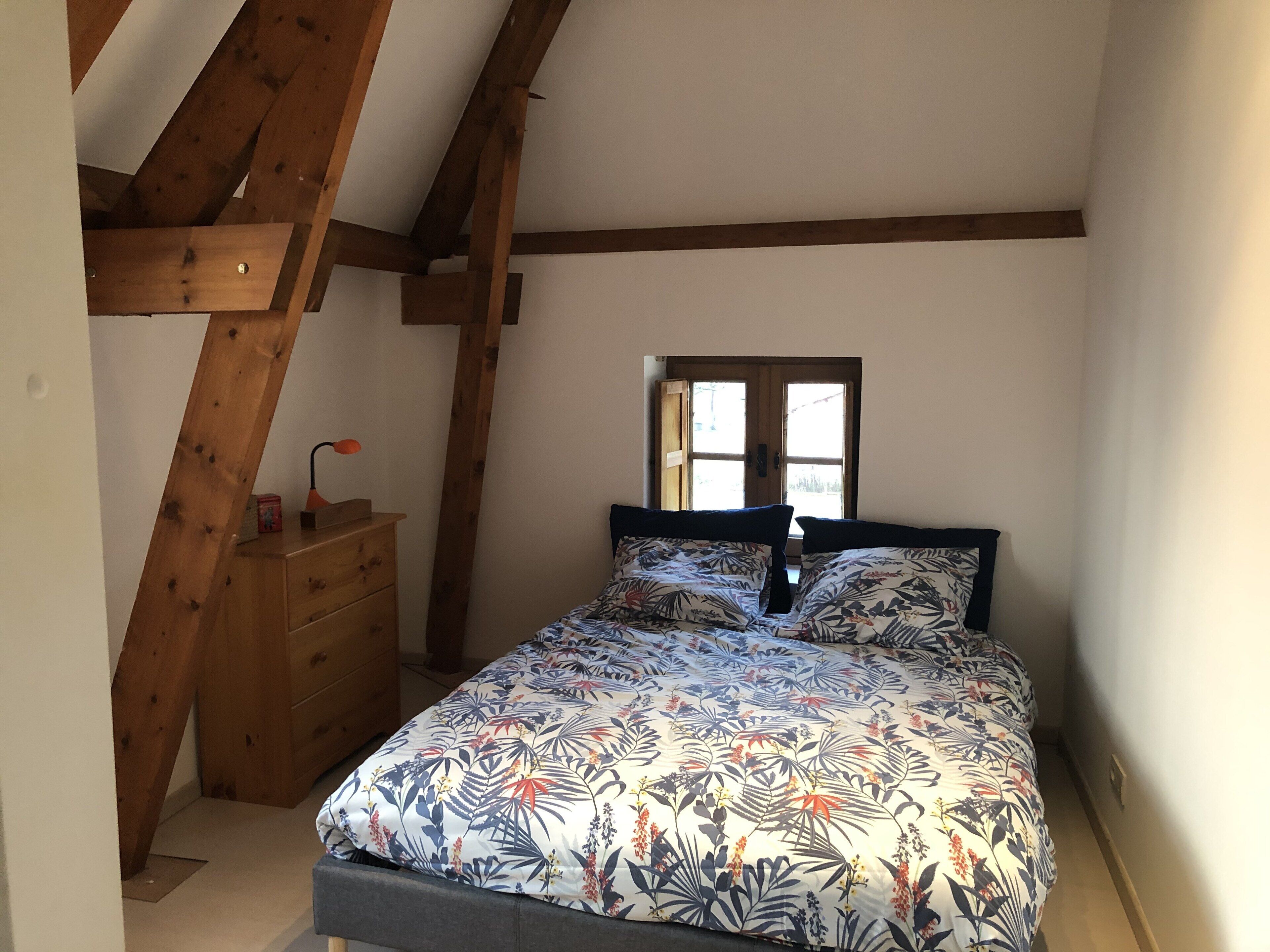 Een slaapkamer met een bed, houten balken, een kapstok en een raam.