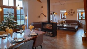 Un salon chaleureux avec une cheminée, un coin repas préparé pour le dîner et un sapin de Noël.