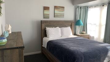 A bedroom with a wooden bed, a nightstand with a lamp, a desk with a decorative item, and two wall art pieces.